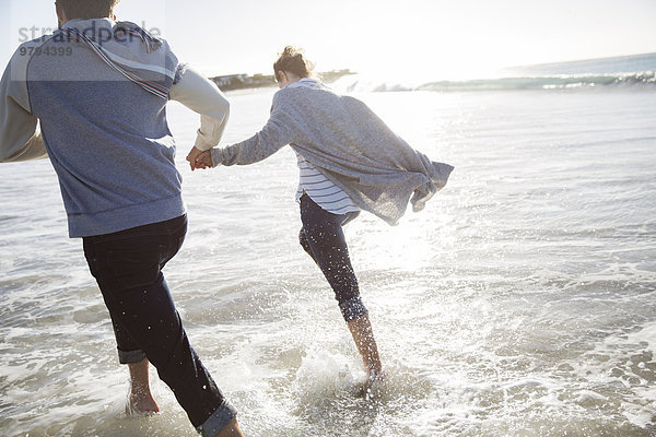 Junges Paar hält sich an den Händen und rennt am Strand.