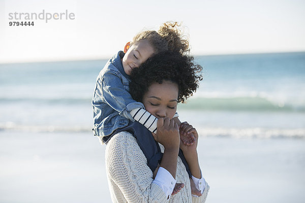 Mutter mit Tochter auf den Schultern am Strand