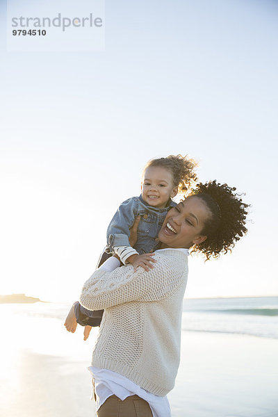 Mutter und Tochter umarmen sich am Strand