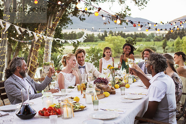 Junges Paar und seine Gäste sitzen bei der Hochzeitsfeier im Garten am Tisch