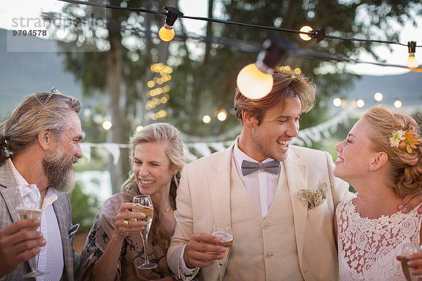 Junges Paar und seine Gäste mit Champagnerflöte bei der Hochzeitsfeier im Garten