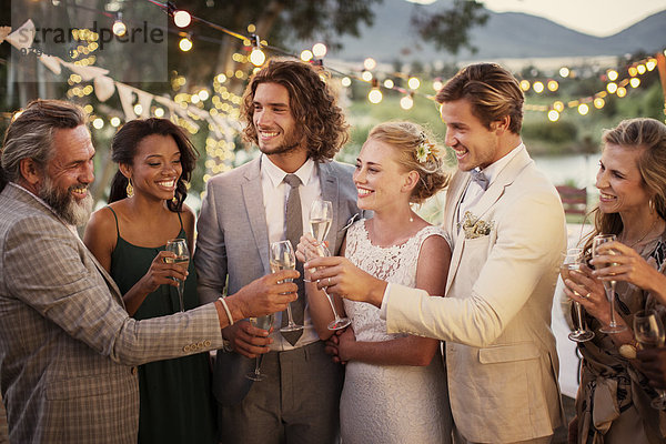 Junges Paar und seine Gäste mit Champagnerflöte bei der Hochzeitsfeier im Garten