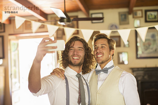 Bräutigam und Trauzeuge beim Selbstfotografieren im Wohnzimmer