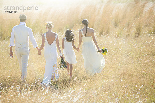 Junges Paar mit Brautjungfer und Mädchen  die auf der Wiese spazieren gehen