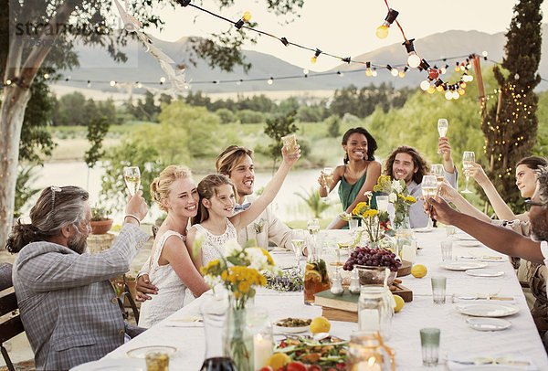 Junges Paar und Gäste toasten mit Champagner bei der Hochzeitsfeier im heimischen Garten