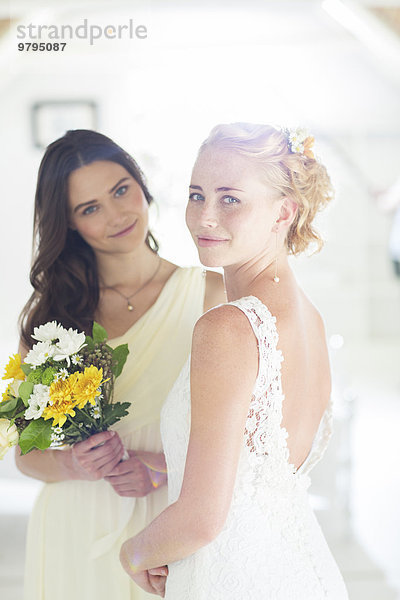 Portrait von Braut und Brautjungfer mit Blumenstrauß im heimischen Zimmer