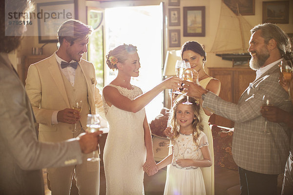 Junges Paar und Gäste toasten mit Champagner bei der Hochzeitsfeier im heimischen Zimmer