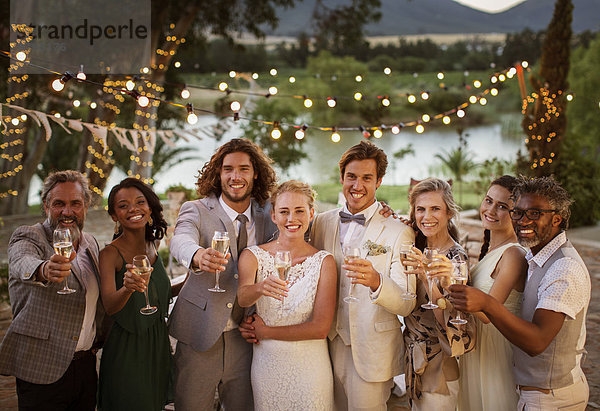 Porträt eines jungen Paares mit Gästetoast mit Champagner bei der Hochzeitsfeier in der Abenddämmerung