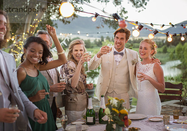 Junges Paar und Gäste toasten mit Champagner bei der Hochzeitsfeier im heimischen Garten