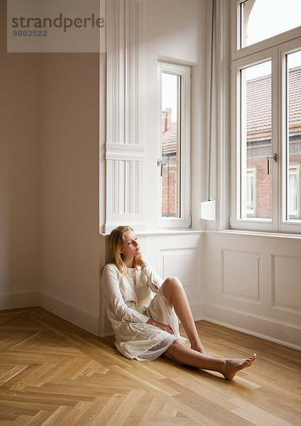 Junge blonde Frau sitzt in Wohnung auf dem Boden