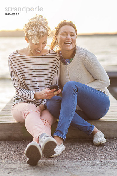 Porträt einer glücklichen Frau  die mit einer Freundin am Pier sitzt.