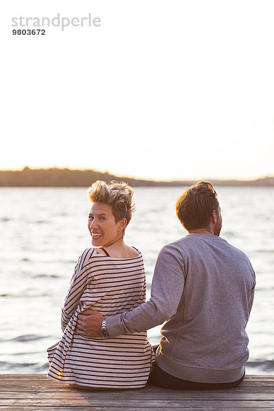 Rückansicht Porträt einer glücklichen Frau  die mit einem Mann am Pier gegen das Meer sitzt.