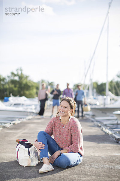Glückliche Frau sitzt am Pier mit Freunden im Hintergrund