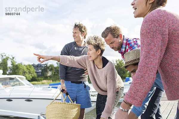 Frau zeigt Freunden etwas  während sie sich auf ein Picknick im Hafen vorbereitet.