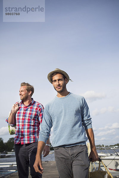 Porträt eines Mannes mit Picknickkorb beim Spaziergang mit einem Freund am Pier