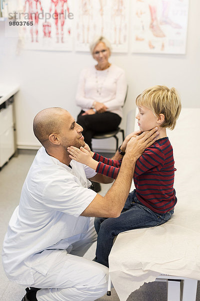 Ältere Frau schaut auf Arzt und Enkel  die sich in der Klinik berühren.