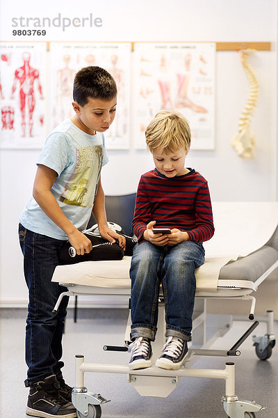 Brüder mit Smartphone am Untersuchungstisch in der orthopädischen Klinik