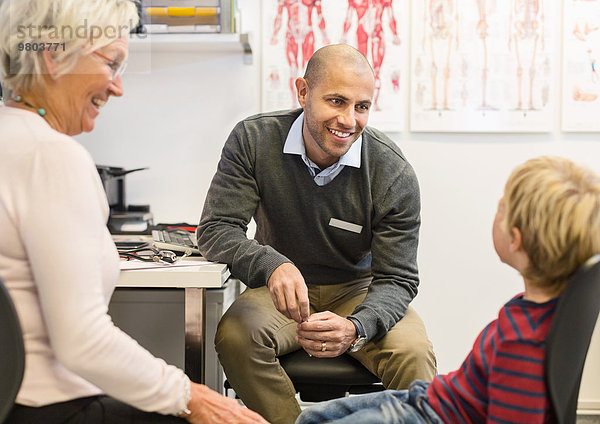 Fröhliche Seniorin beim Blick auf den Enkel im Gespräch mit dem Arzt der Orthopädischen Klinik