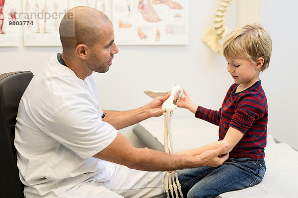 Männlicher Arzt erklärt dem Jungen in der orthopädischen Klinik das Handmodell