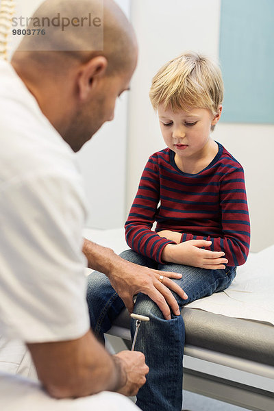 Arzt untersucht Kniereflexe des Jungen in der orthopädischen Klinik