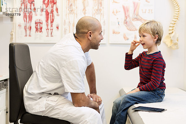 Orthopäde im Gespräch mit dem Jungen auf dem Untersuchungstisch in der Klinik