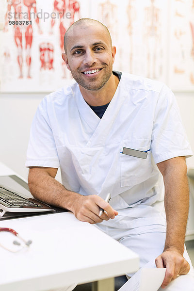 Porträt eines glücklichen orthopädischen Arztes am Schreibtisch in der Klinik