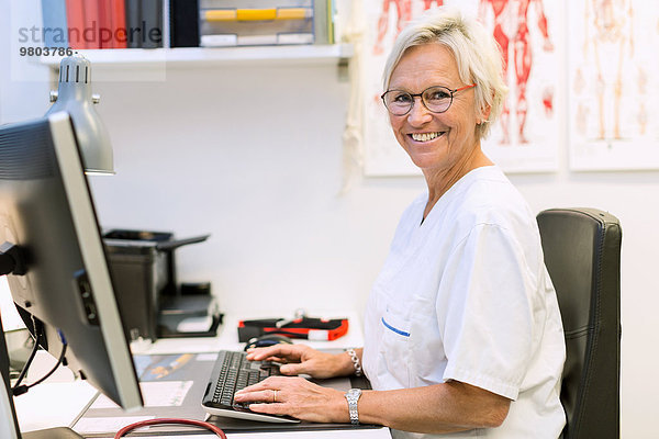Porträt eines glücklichen leitenden orthopädischen Chirurgen mit Computer am Schreibtisch in der Klinik