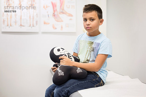 Porträt eines Jungen mit Skelettfüllung auf dem Untersuchungstisch in der orthopädischen Klinik