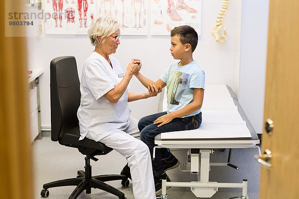 Senior-Orthopädin untersucht die Hand des Jungen in der Klinik