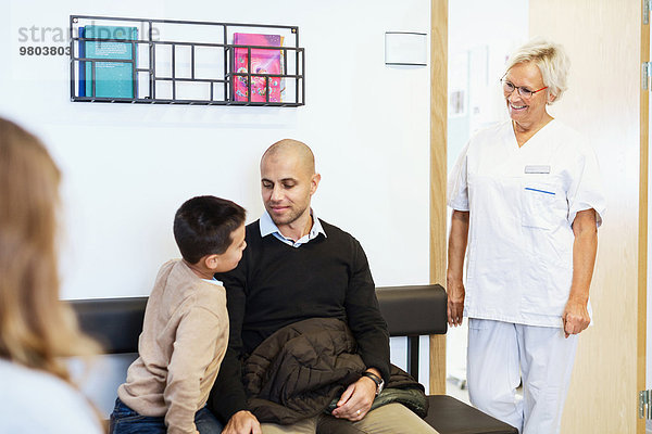 Glückliche Krankenschwester im Gespräch mit Patienten im Wartezimmer der orthopädischen Klinik