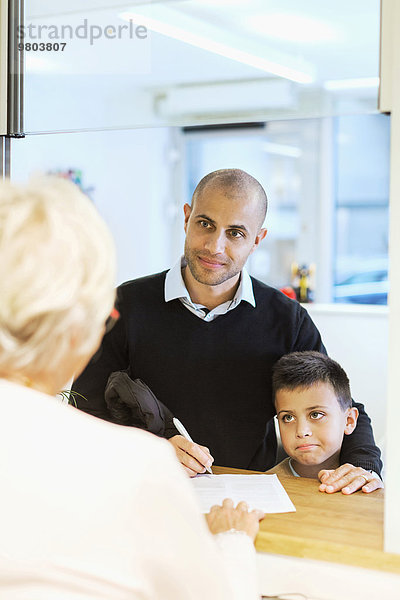 Vater und Sohn beim Ausfüllen von Formularen in der orthopädischen Praxis