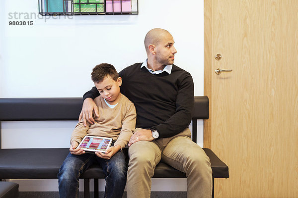 Vater und Sohn sitzen im Wartezimmer der orthopädischen Klinik