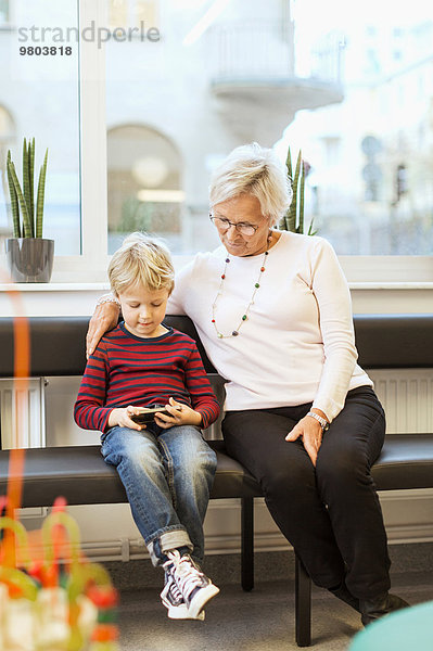 Großmutter und Enkel mit Smartphone im Wartezimmer der Orthopädischen Klinik