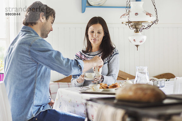 Glücklicher Mann serviert Kaffee für die Frau am Frühstückstisch