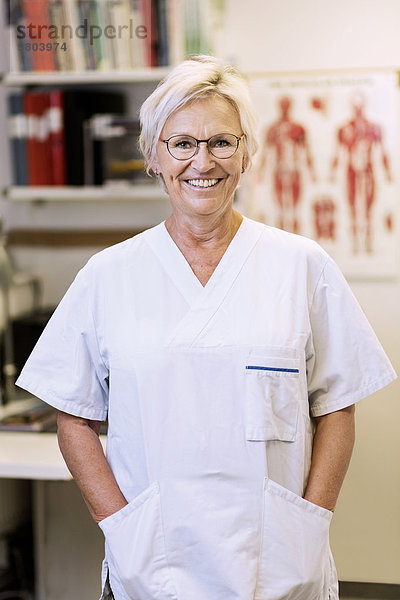 Porträt eines glücklichen leitenden orthopädischen Chirurgen mit Händen in den Taschen in der Klinik