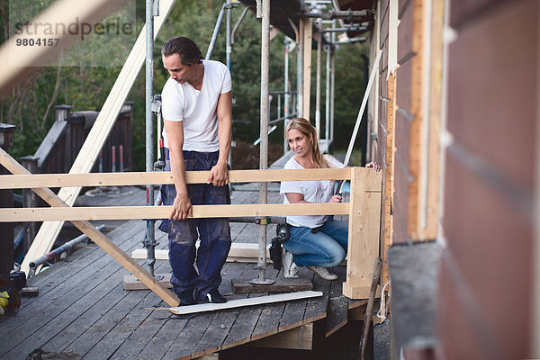 Volle Länge des Paares  das auf der Veranda des zu renovierenden Hauses arbeitet.