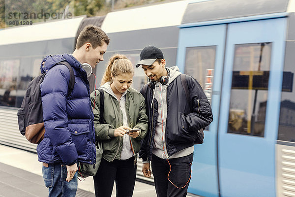 Multiethnische Universitätsstudenten mit dem Handy an der U-Bahn-Station