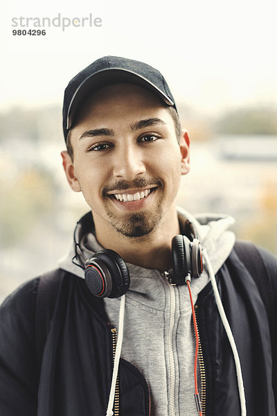 Porträt eines glücklichen Studenten mit Kopfhörern um den Hals im Freien