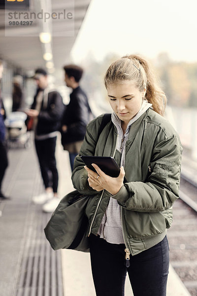 Junge Studentin mit digitalem Tablett in der U-Bahn-Station mit Freunden im Hintergrund