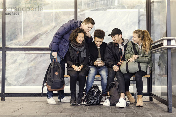 Gruppe von Studenten  die gemeinsam an der U-Bahn-Station ein Smartphone benutzen
