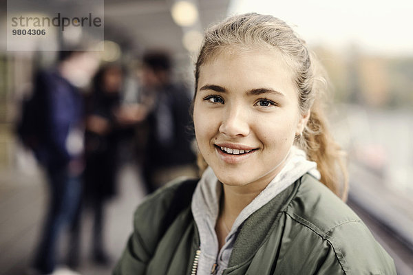 Porträt eines lächelnden Studenten an der U-Bahn-Station mit Freunden im Hintergrund