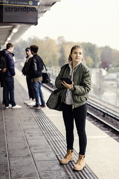 Volle Länge der Studentin mit digitalem Tablett an der U-Bahn-Station mit Freunden im Hintergrund