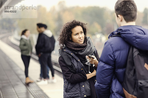 Ein Paar spricht auf dem U-Bahn Bahnsteig  während Freunde im Hintergrund sitzen