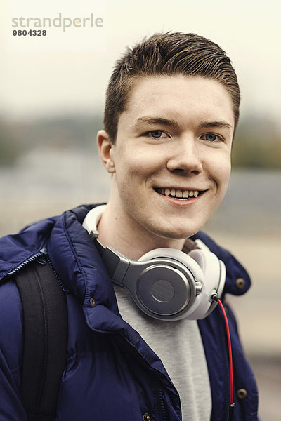 Porträt eines glücklichen Studenten mit Kopfhörer um den Hals im Freien