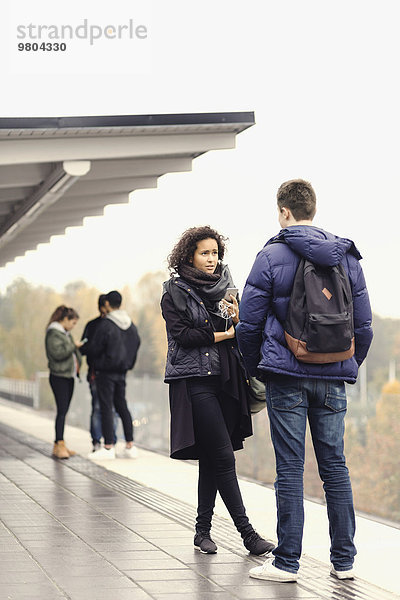 Ein Paar spricht auf dem Bahnsteig  während Freunde im Hintergrund stehen.