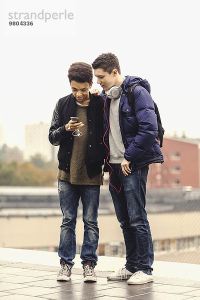 Volle Länge der männlichen Studenten  die das Handy benutzen  während sie in der U-Bahn warten.