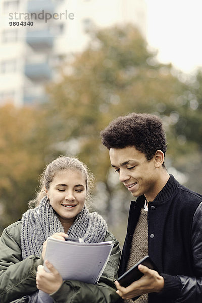 Lächelnde Studenten diskutieren über Notizen im Freien