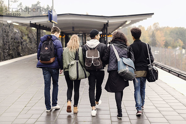 Durchgehende Rückansicht der Studenten  die gemeinsam auf dem U-Bahn Bahnsteig gehen.