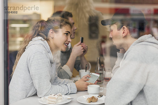 Blick auf ein junges Paar beim Telefonieren im Cafe durchs Glas