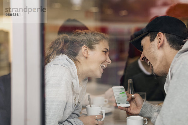 Blick auf das glückliche junge Paar mit Smartphone im Cafe durch Glas